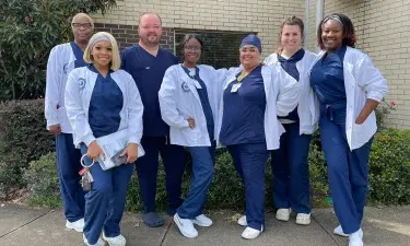 Seven Herzing University MSN Direct Entry nursing students in scrubs smiling while posing for photo